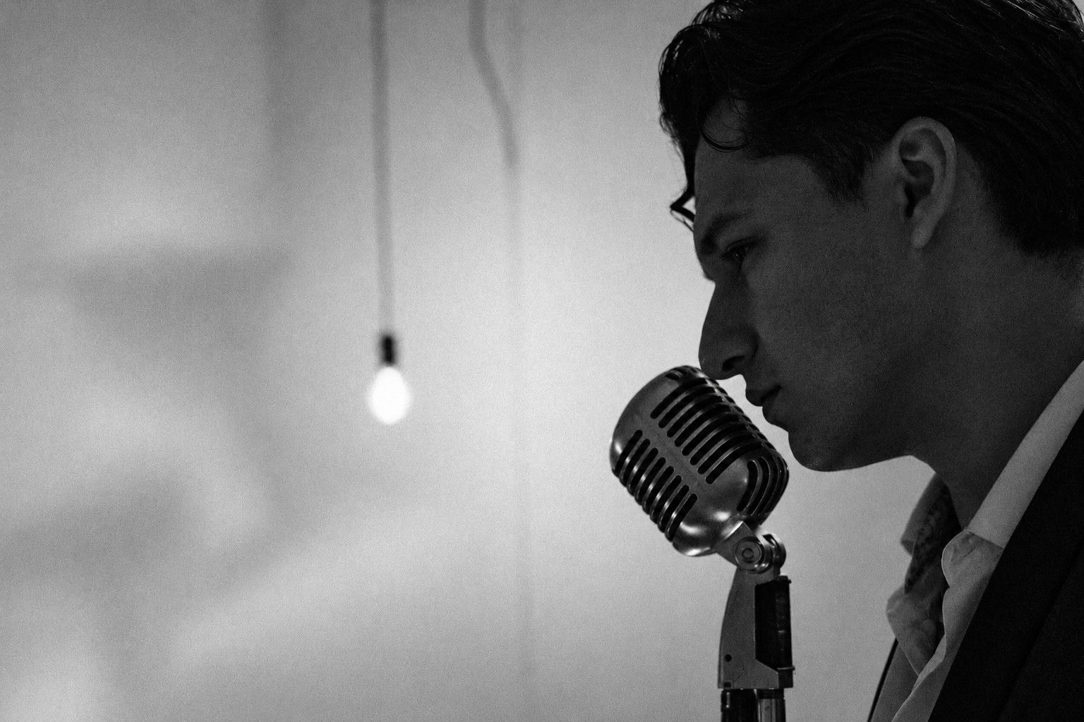 Diego Martinez in profile at a vintage microphone, a single bulb glowing behind him