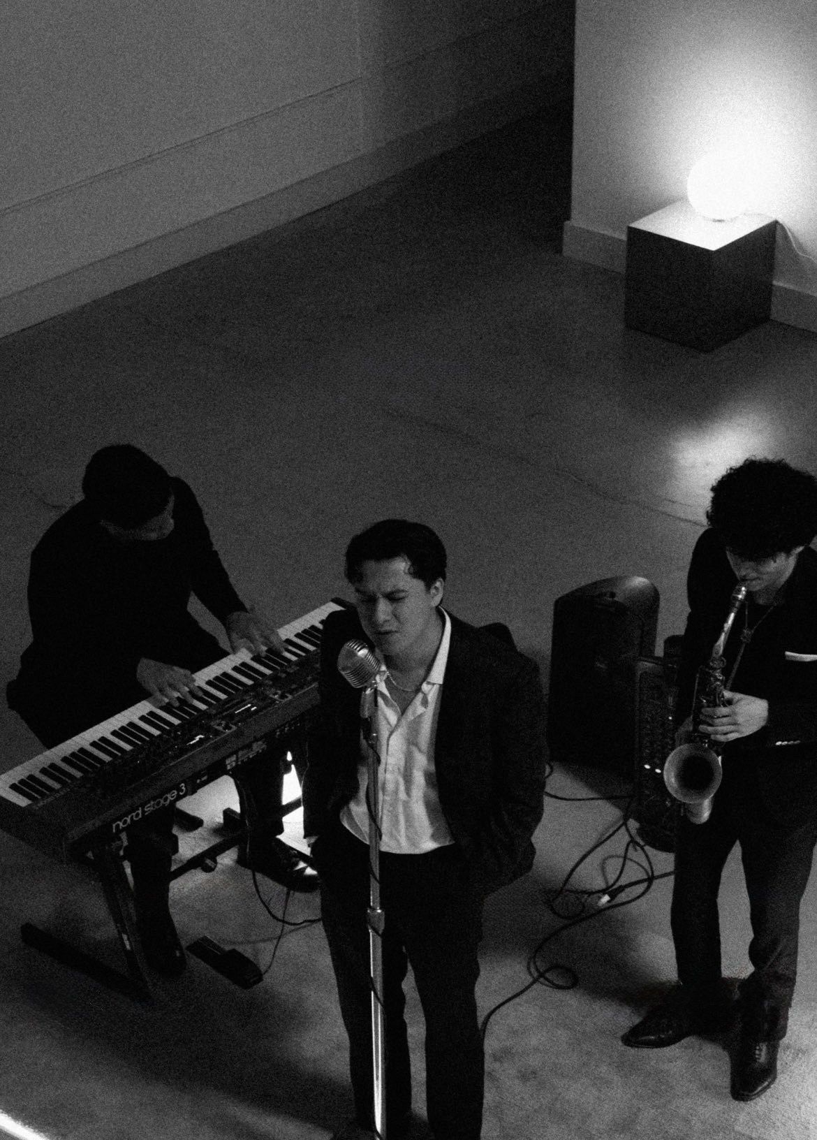 Overhead view of Diego singing with a keyboardist and saxophonist in a gallery space